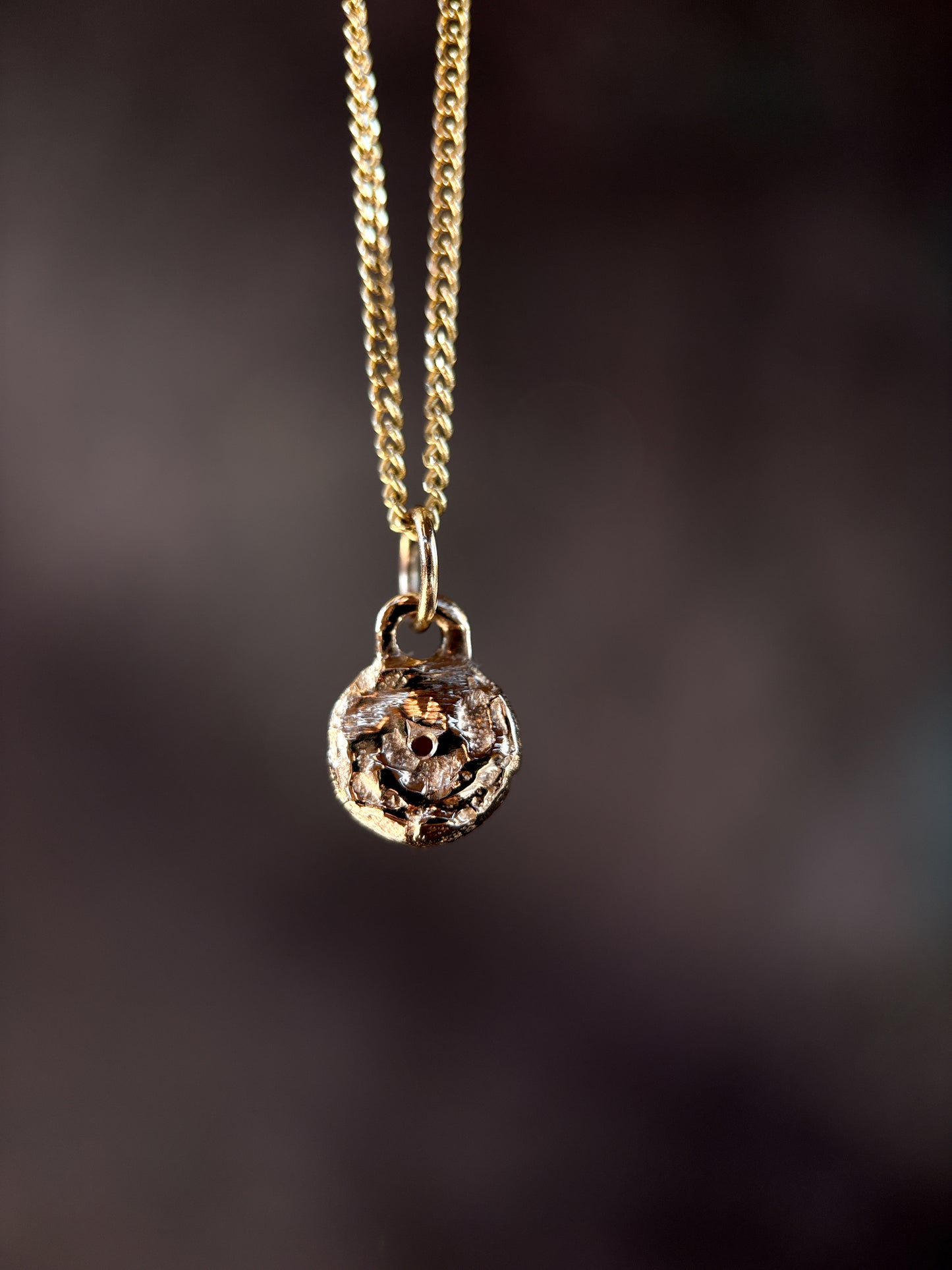 Gold necklace with a round pendant on a dark background
