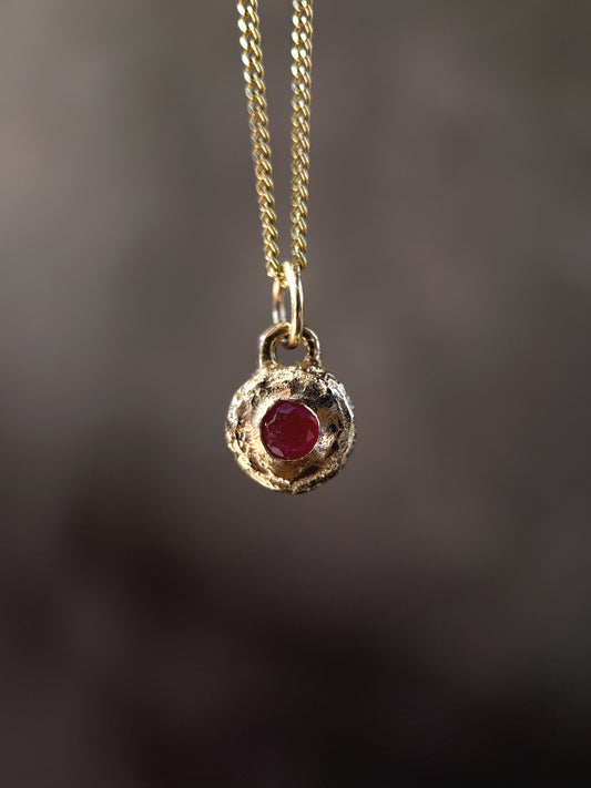 Gold necklace with a red gemstone pendant on a dark background