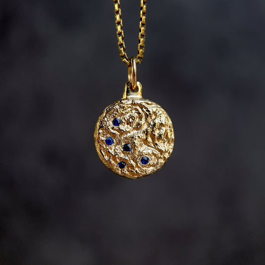 Gold necklace with a round pendant featuring blue stones on a dark background