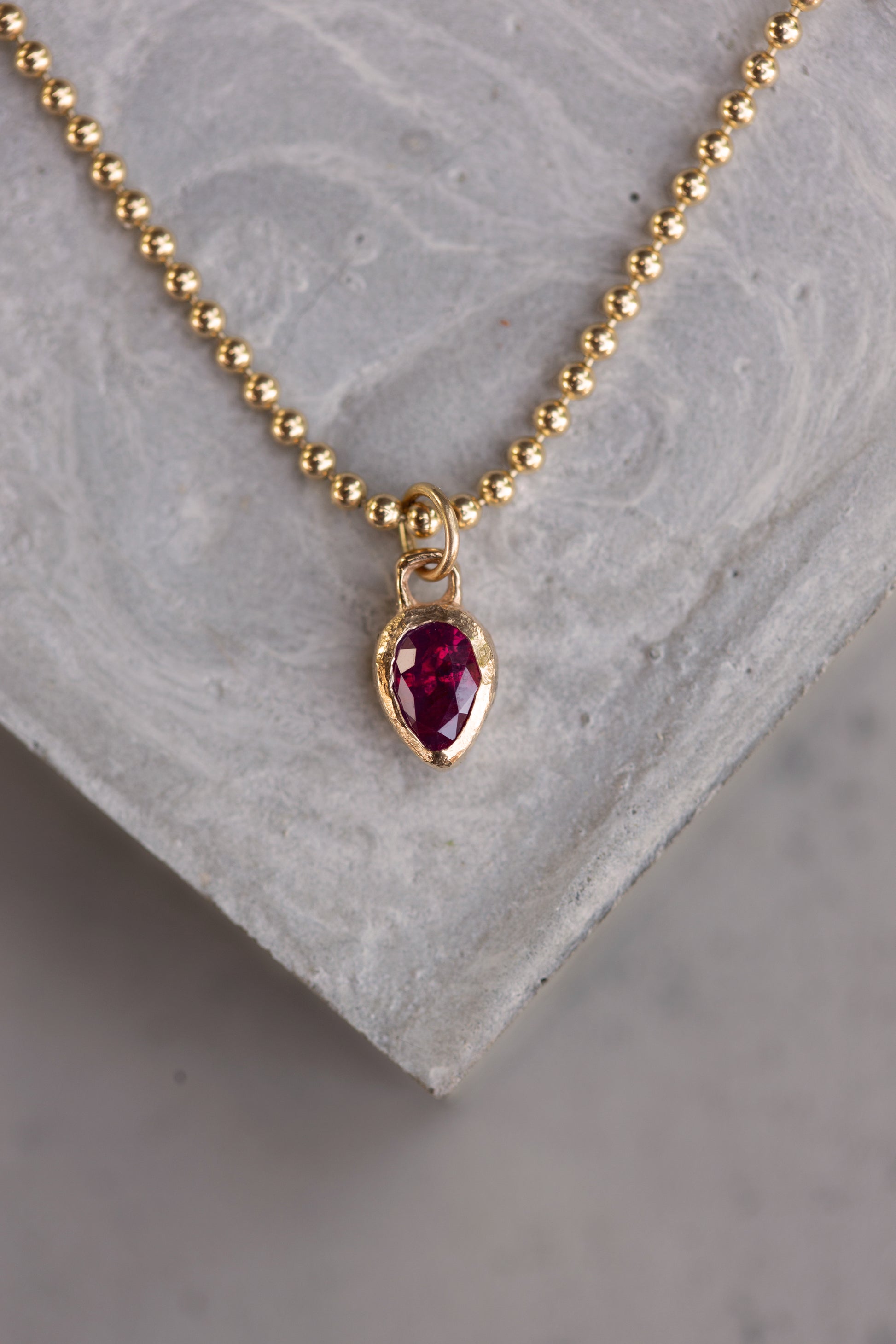 Gold necklace with a red gemstone pendant on a gray stone surface