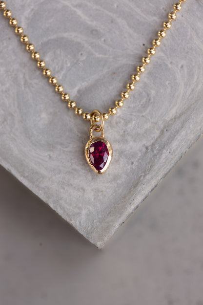 Gold necklace with a red gemstone pendant on a gray stone surface