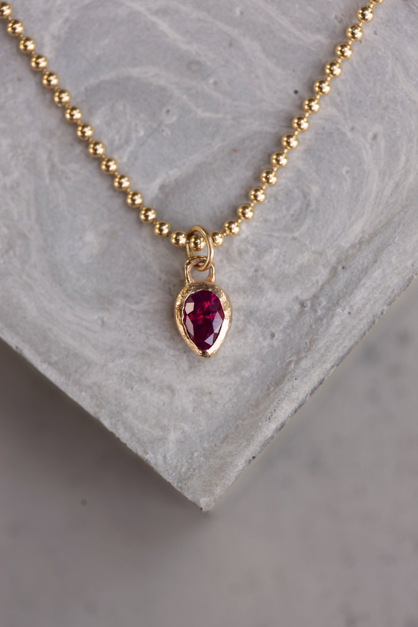 Gold necklace with a red gemstone pendant on a gray stone surface