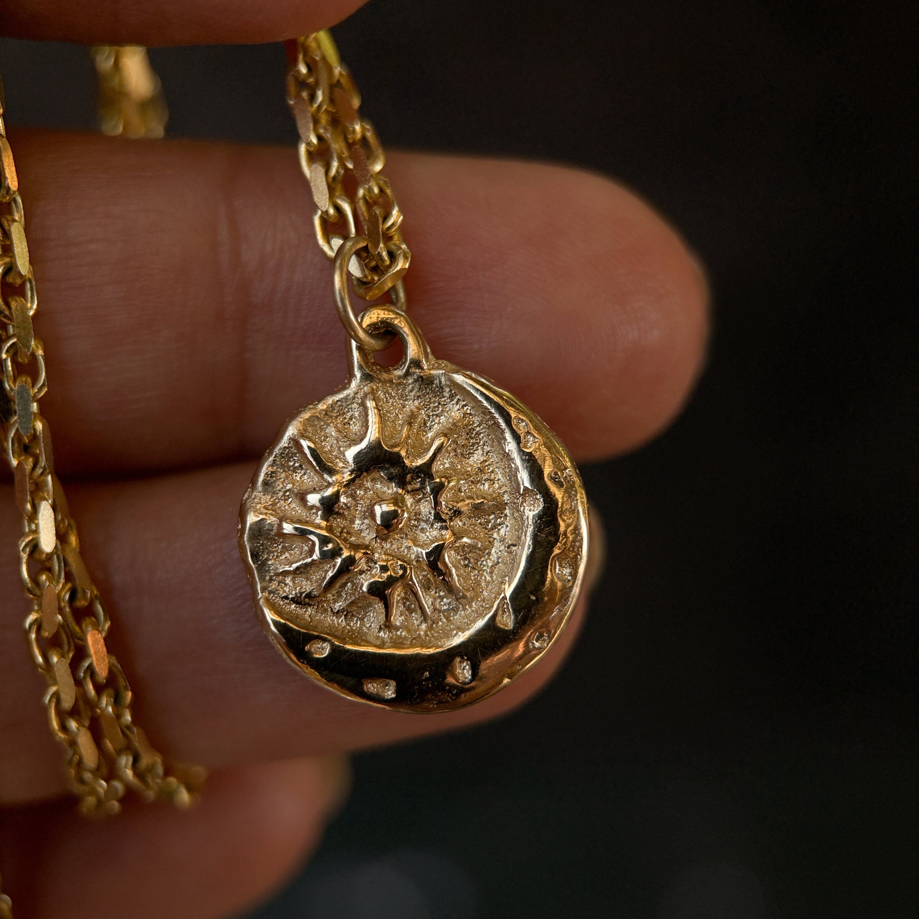 Gold necklace with a detailed pendant held between fingers against a dark background