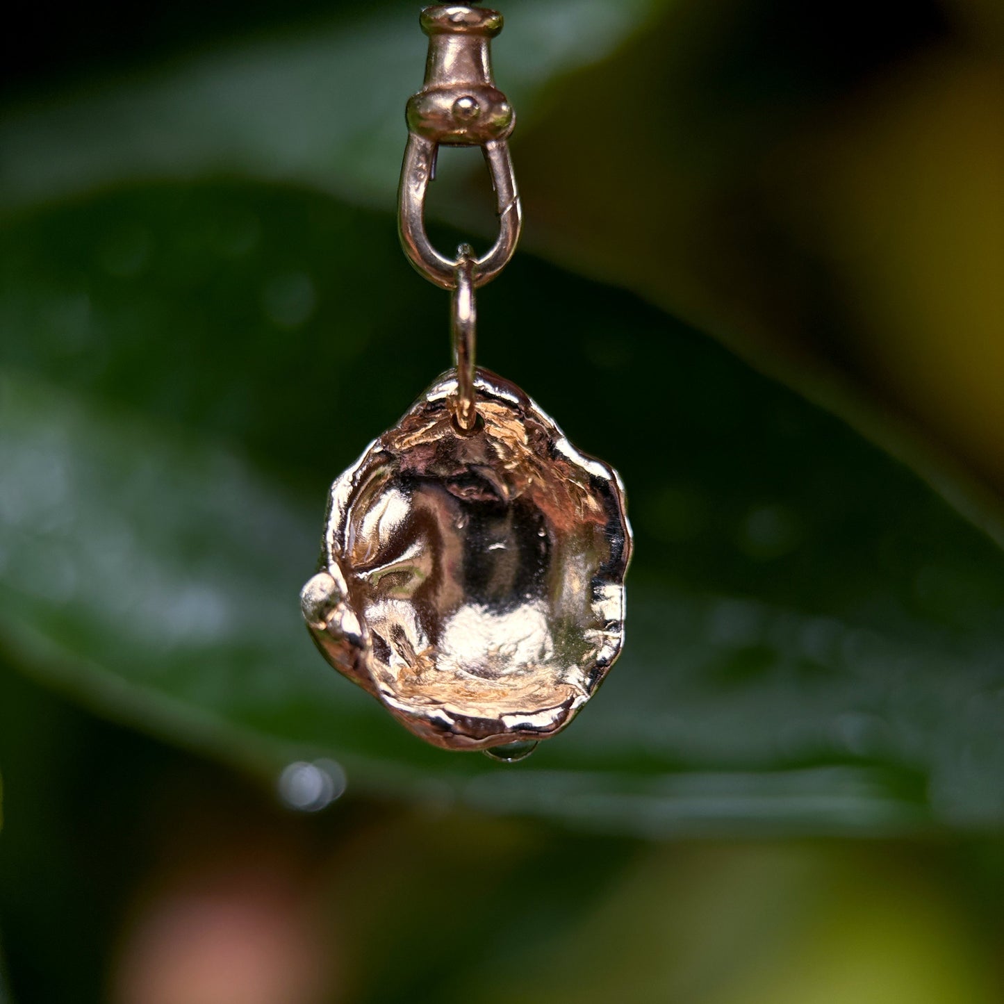 Gold pendant with a textured design on a blurred green background